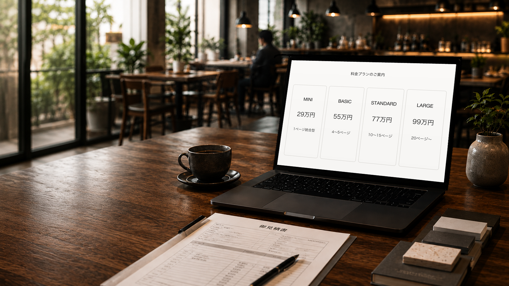 モダンなカフェでPC画面にMINI・BASIC・STANDARD・LARGEの料金プランが表示され、手前に見積書が置かれているイメージ